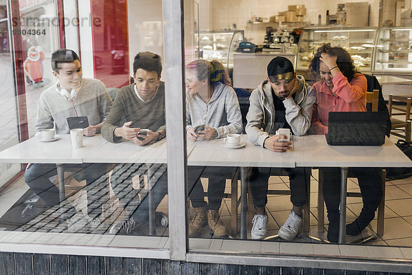 Multiethnische Freunde  die Technologien bei Tisch in der Cafeteria nutzen