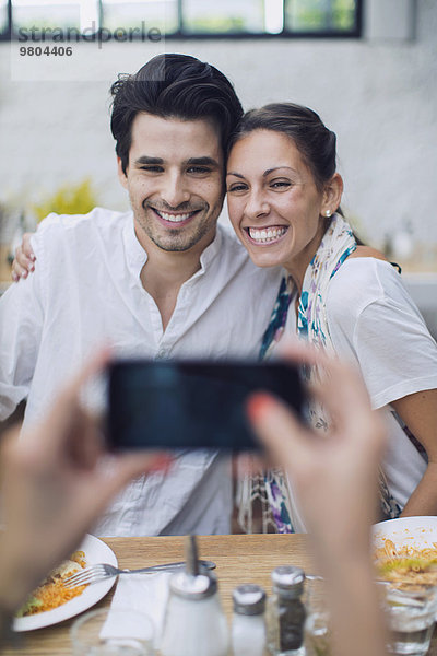 Freund fotografiert Paar durch Smartphone im Cafe