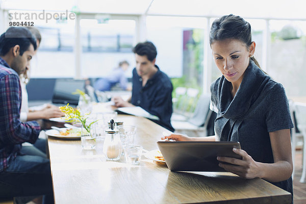 Frau mit digitalem Tablett mit Freunden im Hintergrund im Cafe
