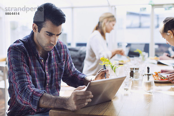 Serious Mann mit digitalen Tablet mit Freunden im Hintergrund im Cafe