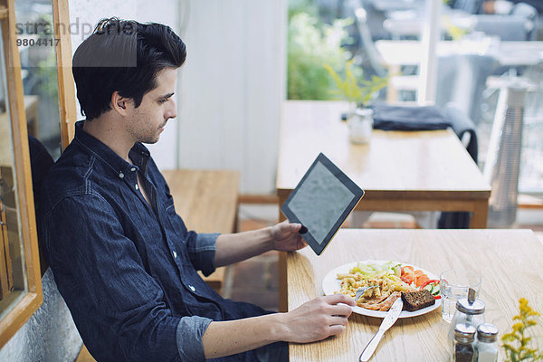 Mann mit digitalem Tablett beim Mittagessen im Cafe