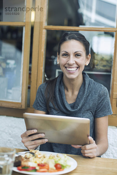 Porträt einer glücklichen Frau mit digitalem Tablett beim Mittagessen im Cafe