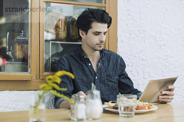 Mann mit digitalem Tablett beim Mittagessen im Cafe