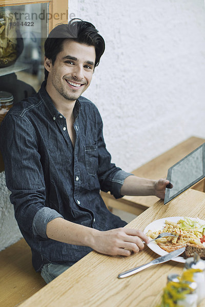 Porträt eines glücklichen Mannes mit digitalem Tablett beim Mittagessen im Cafe