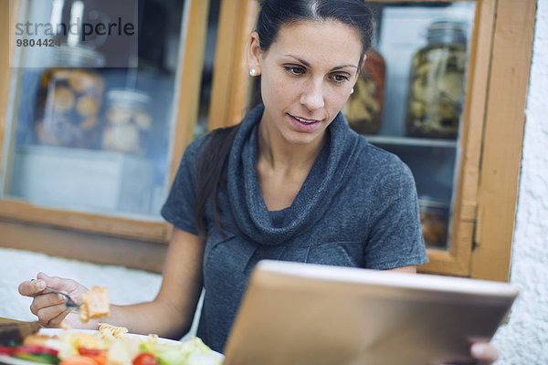 Frau mit digitalem Tablett beim Mittagessen im Cafe