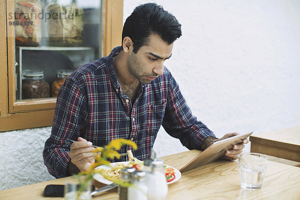 Mann mit digitalem Tablett beim Mittagessen im Restaurant