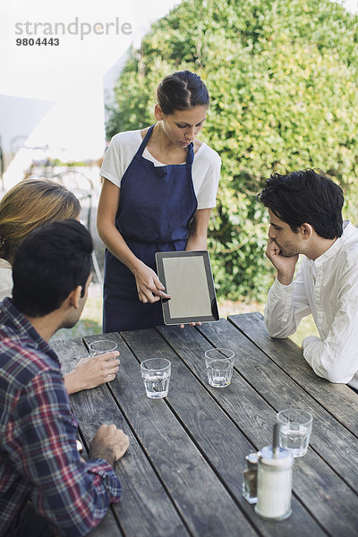 Kellnerin  die den Leuten im Außenrestaurant das Menü durch ein digitales Tablett zeigt.