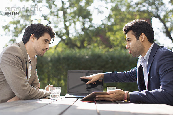 Geschäftsmann im Gespräch mit männlichen Kollegen über Laptop im Outdoor-Café