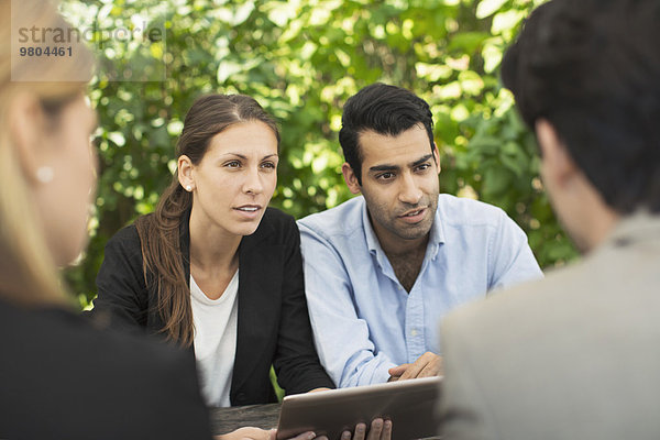 Business-Paare diskutieren im Outdoor-Café über den Einsatz von digitalen Tabletts