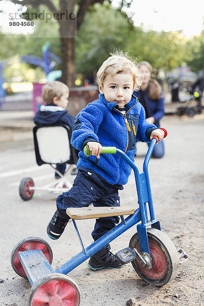 Porträt eines Jungen  der mit einem Dreirad auf dem Spielplatz spielt.