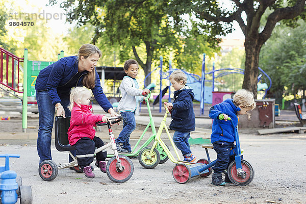 Lehrerin  die dem Mädchen hilft  auf dem Spielplatz Dreirad zu fahren.