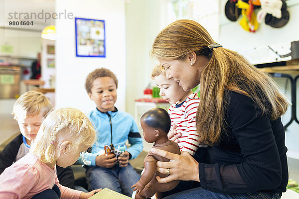 Lehrer und Kinder mit Spielzeug im Kindergarten