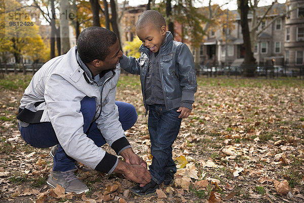 Junger Mann bindet Kleinkind Söhne Schnürsenkel im Park
