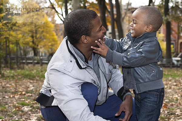 Männliches Kleinkind berührt Vatergesicht im Herbstpark