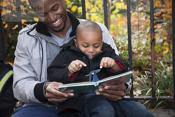 Männliches Kleinkind und Vater lesen Märchenbuch im Park