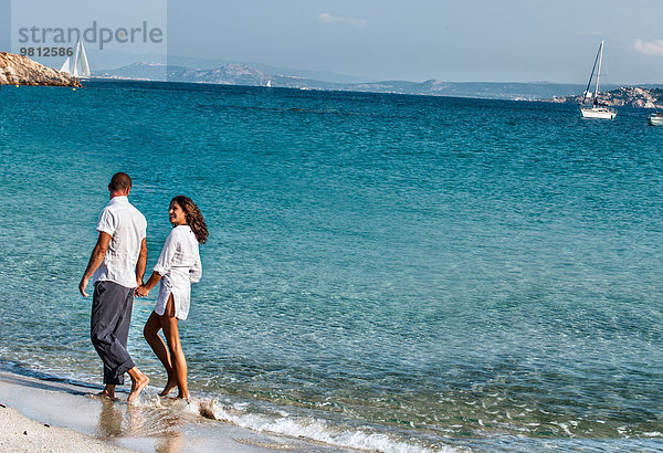 Ein Paar geht Hand in Hand am Strand entlang.