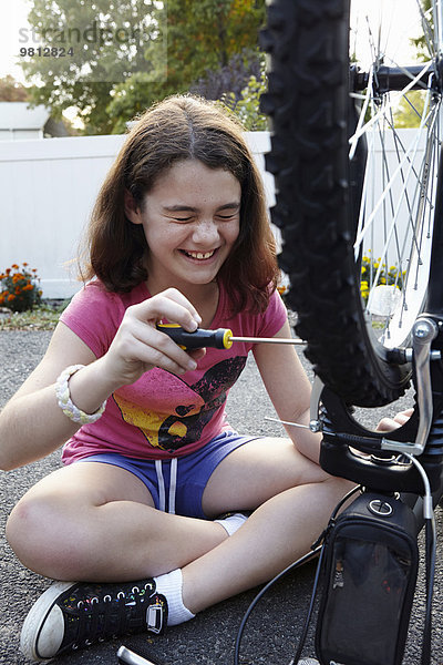 Lachendes Mädchen repariert Fahrrad auf der Einfahrt
