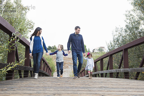 Paar und zwei Kinder schlendern Hand in Hand über die Parkbrücke