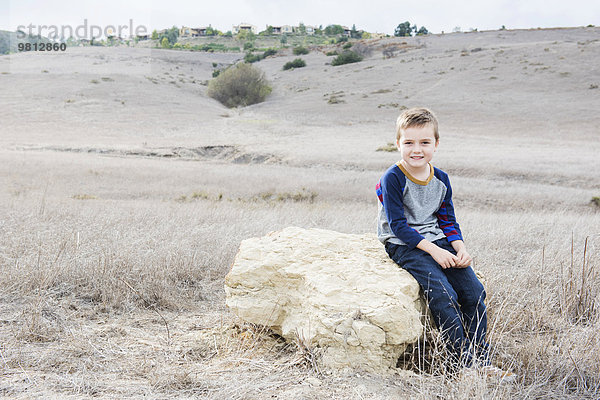 Porträt eines Jungen auf einem Felsen sitzend