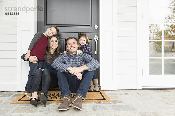 Porträt von Eltern und zwei Kindern  die vor der Haustür sitzen