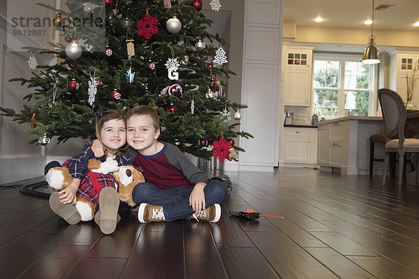 Bildnis des Bruders mit Arm um die Schwester vor dem Weihnachtsbaum