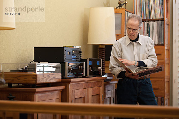 Senior Mann liest Schallplattencover im Wohnzimmer