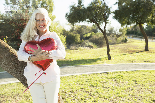 Senior Frau umarmt roten herzförmigen Ballon  Hahn Park  Los Angeles  Kalifornien  USA