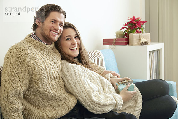 Portrait eines jungen Paares auf Sofa mit Weihnachtsgeschenk