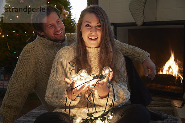 Junges Paar im Wohnzimmer mit beleuchteten Weihnachtslichtern