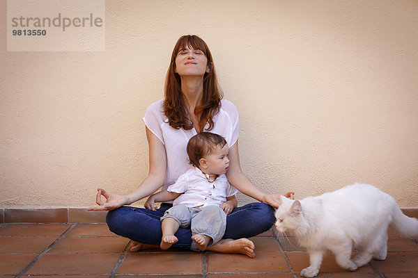 Porträt einer mittleren erwachsenen Frau  die Yoga mit ihrer kleinen Tochter auf dem Küchenboden praktiziert.