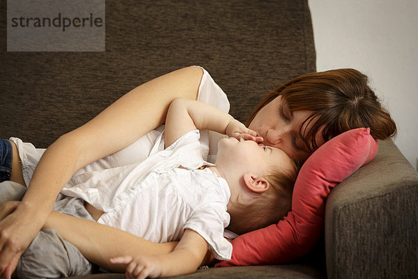 Mittlere erwachsene Frau  die ihre Tochter auf dem Sofa küsst.