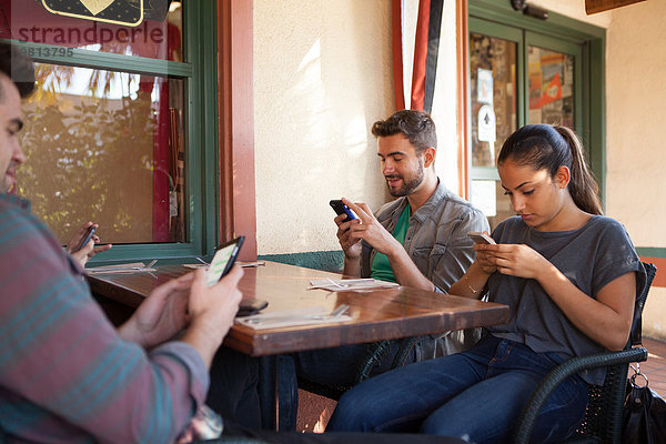 Vier Freunde texten individuell auf Smartphones im vegetarischen Restaurant