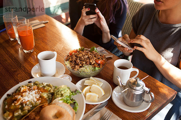 Ausschnittaufnahme von weiblichen Freunden  die auf Smartphones im vegetarischen Restaurant texten.