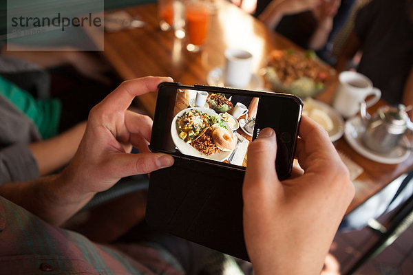 Ausschnitt eines Mannes  der das Essen in einem vegetarischen Restaurant fotografiert.