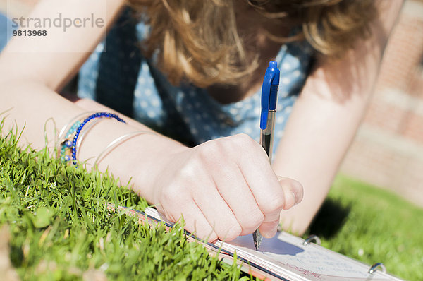Ausschnitt aus der Nähe von Teenager-Mädchen  die in einem Tagebuch im Park schreiben.