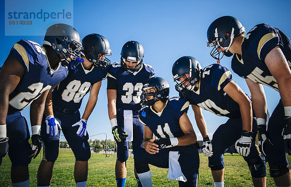 Teenager und junge männliche American-Football-Teams treffen und planen beim Training