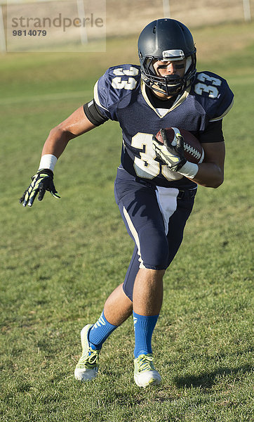 Teenager American Footballer läuft mit Ball auf dem Spielfeld