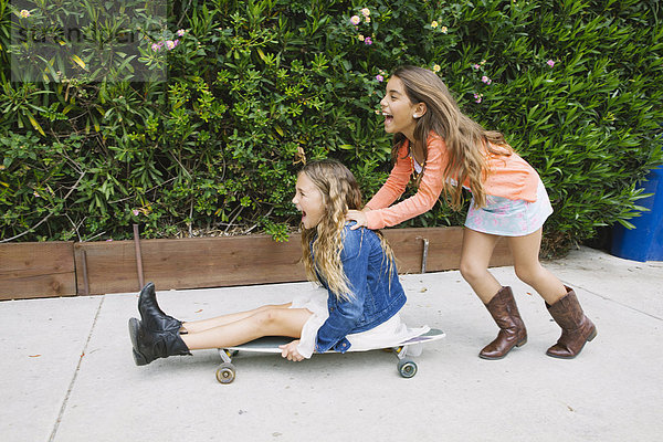 Mädchen schiebt Freund auf Skateboard