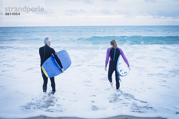 Vater und Tochter mit Surfbrettern im Meer