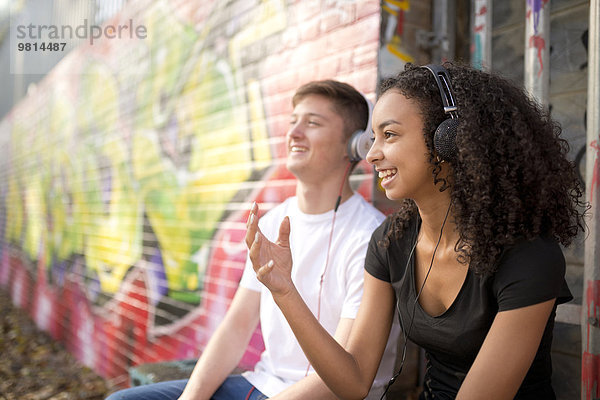 Teenager-Paar hört mp3-Player gegen die Wand mit Graffiti