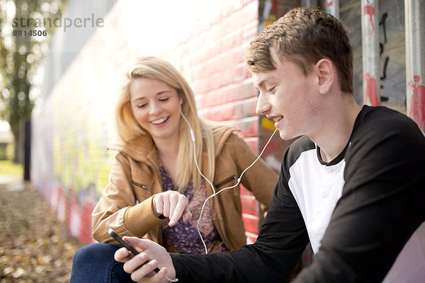 Teenager-Paar hört mp3-Player gegen die Wand mit Graffiti