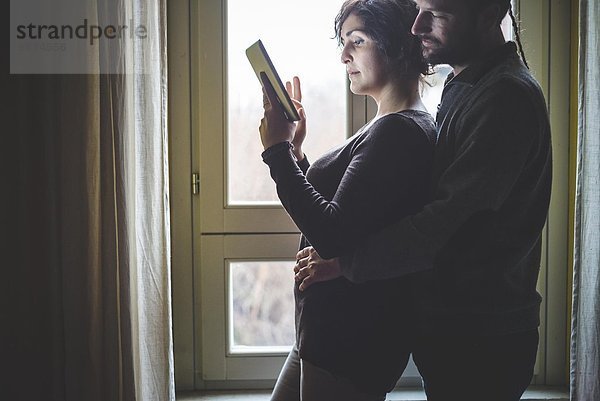 Paar neben dem Fenster stehend  mit digitalem Tablett