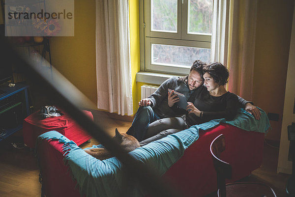 Paar sitzt auf dem Sofa und schaut auf das digitale Tablett.