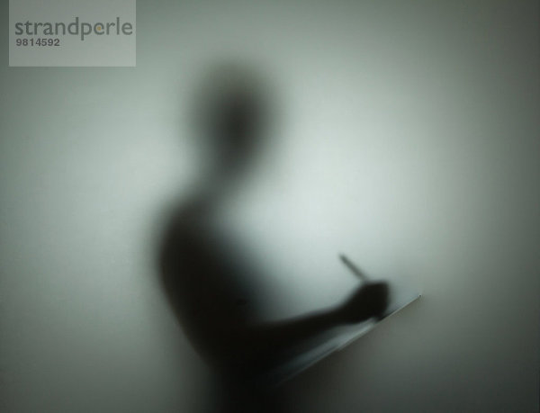 Silhouette der Person mit Stift und Klemmbrett  hinter Glas