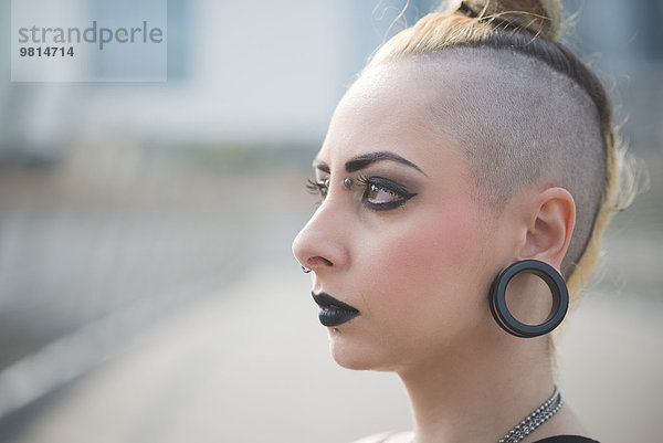 Porträt einer jungen Punkerin mit Ohrläppchenpiercing und rasiertem Kopf
