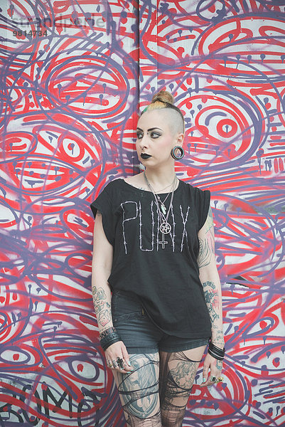 Porträt einer jungen Punkerin  die sich an eine Graffiti-Wand lehnt.