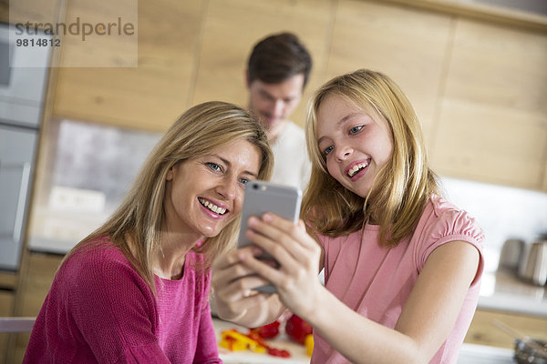 Mittlere erwachsene Frau und Tochter nehmen Smartphone Selfie im Esszimmer