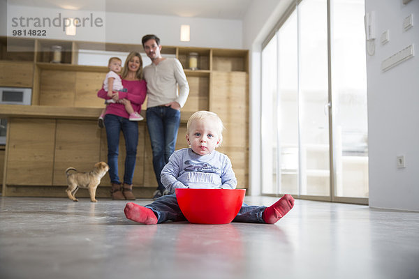 Familie beobachtet männliches Kleinkind mit Schüssel auf dem Boden des Esszimmers