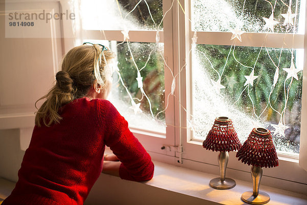 Mutter schaut aus dem Fenster mit Weihnachtsschmuck