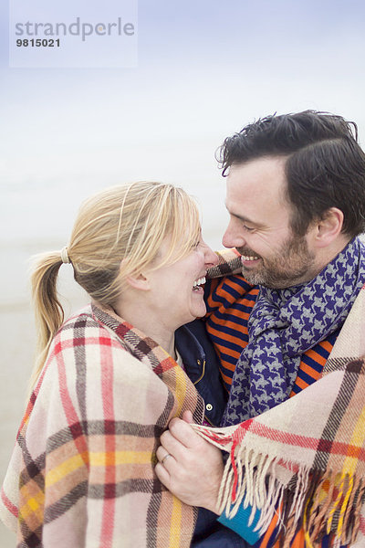 Paar am Strand  lachend und warmhaltend unter der Decke